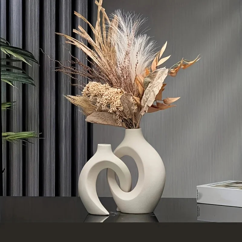 White abstract vase with dried flowers on a reflective surface against a gray textured wall.